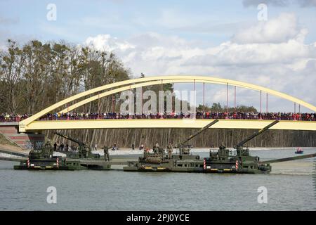 Finowfurt, Deutschland. 30. März 2023. Zuschauer, die auf einer Fußgängerbrücke stehen, blicken auf M3 Amphibienfahrzeuge, die eine Brücke auf dem Wasser unter ihnen bilden, während der britische König das englisch-deutsche Brückenbrücke-Bataillon 130. in Finowfurt besucht (nicht gesehen). Vor seiner Krönung im Mai 2023 werden der britische König und die königliche Frau Deutschland für drei Tage besuchen. Kredit: Jens Schlueter/AFP Pool/dpa/Alamy Live News Stockfoto