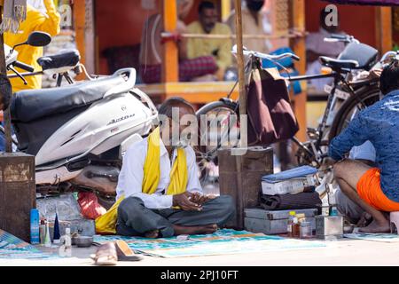 Haridwar, Indien - Okt. 2022: Straßenfriseur wartet mit Rasier- und Haarschneideausrüstung in der Nähe des ganges in haridwar auf den Kunden. Stockfoto