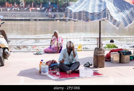 Haridwar, Indien - Okt. 2022: Straßenfriseur wartet mit Rasier- und Haarschneideausrüstung in der Nähe des ganges in haridwar auf den Kunden. Stockfoto