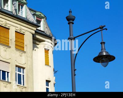 Lampenkopf im Retro-Stil. Nahaufnahme. Ansicht aus niedrigem Winkel. Stuckfassade dahinter. Glaslinse. Graue Lampenabdeckung. Mansardendach und Dachfenster Stockfoto