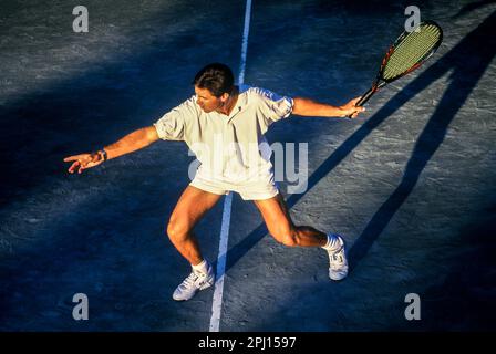JUNGER MÄNNLICHER TENNISSPIELER MIT VORHÄNGESCHWINGUNG AUF DEM SANDTENNISPLATZ Stockfoto