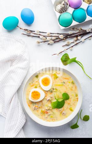 Traditionelle polnische Sauersuppe Zurek mit Rochenmehl, g und Gemüse auf dem Küchentisch mit Osterdekoration Stockfoto