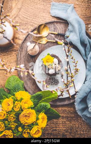 Ostertisch mit Frühlingsblumen und Besteck auf Holztisch. Osterfeiertag Im Frühling Stockfoto