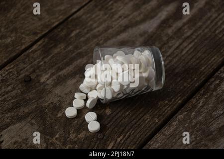 Glasbecher mit weißen runden Tabletten auf dem Tisch Stockfoto