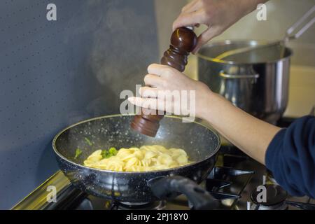 Bild einer Frauenhände, die frisch gekochte Pasta in einer Pfanne mit einer Pfeffermühle würzen Italienische kulinarische Tradition. Stockfoto