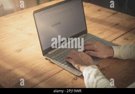 Männerhände, die zu Hause auf einem Laptop tippen, auf einem Holztisch und bei sanftem Sonnenlicht Stockfoto