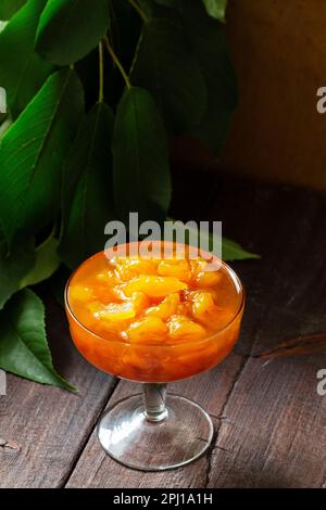 Gelbe Kirschmarmelade mit Zitrone und Vanille in einer Glasschüssel auf Holzhintergrund. Stockfoto