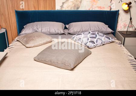 Innenausstattung eines Schlafzimmers mit einem großen Bett mit einem samtblauen Kopfteil, weichen Kissen und einem Wollkaromuster. Stockfoto