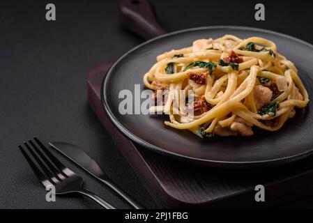 Köstliche Pasta mit Spinat, sonnengetrockneten Tomaten, Käse, Zwiebeln, Gewürzen und Kräutern auf dunklem Betonhintergrund Stockfoto