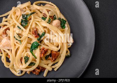 Köstliche Pasta mit Spinat, sonnengetrockneten Tomaten, Käse, Zwiebeln, Gewürzen und Kräutern auf dunklem Betonhintergrund Stockfoto