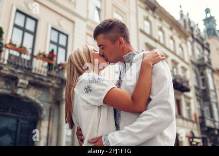 Ein verliebtes junges Paar, das in der Altstadt von Lemberg in traditionellen ukrainischen Hemden spaziert. Mann und Frau umarmen und küssen sich draußen Stockfoto