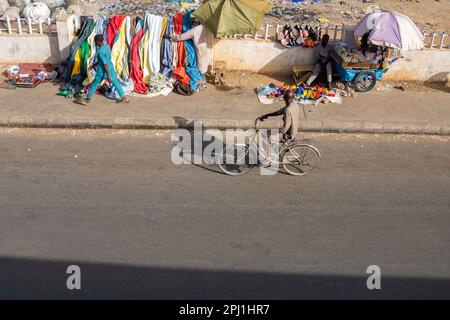 Ein Mann fährt Fahrrad, während er Händler auf einem Markt in Kano, Nigeria, ansieht. Stockfoto