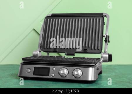 Moderner elektrischer Grill mit offenem Deckel auf grünem Tisch Stockfoto