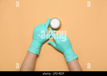 Kosmetologe in Gummihandschuhen mit cremefarbenem beigefarbenem Hintergrund Stockfoto