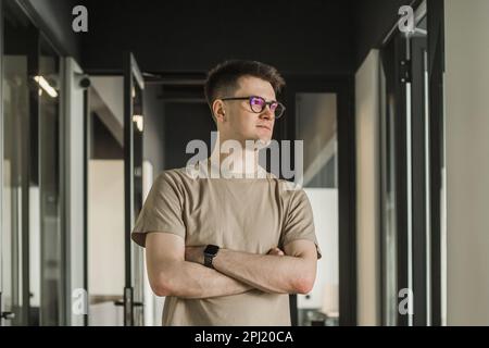 Porträt mit Porträt ein kluger Geschäftsmann mit Brille sitzt am Schreibtisch in einem modernen Büro, schaut in die Kamera, selbstbewusster, zufriedener Freiberufler posiert Stockfoto