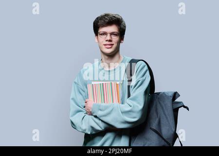 Porträt eines jungen männlichen College-Studenten mit Brille und Rucksack auf grauem Hintergrund Stockfoto