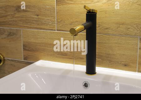 Schwarzer goldener Wasserhahn mit weißem Keramikwaschbecken Stockfoto