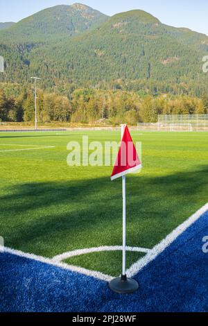 Fußballfeld. Foto eines Sportplatzes mit grünem synthetischem Gras und weißer Linie. Detail der Ecke mit roter Flagge. Niemand, selektiver Fokus, Straßenpho Stockfoto