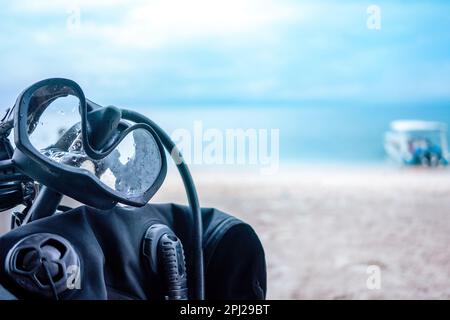 Hintergrund einer Tauchschule. Schwarze Taucherbrille hängt im Vordergrund an der Tauchausrüstung. Im unscharfen Hintergrund ist Meer, blauer Himmel, Stockfoto