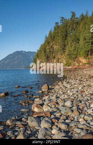 Harrison Lake und Berge bei Sonnenuntergang BC Canada. Flussstein im Wasser, Sommer Natur Hintergrund. Wasser und Steine. Große Steine am Ufer. Verfahrweg p Stockfoto