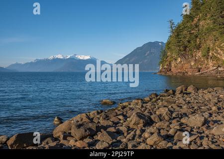 Harrison Lake und Berge bei Sonnenuntergang BC Canada. Flussstein im Wasser, Sommer Natur Hintergrund. Wasser und Steine. Große Steine am Ufer. Verfahrweg p Stockfoto