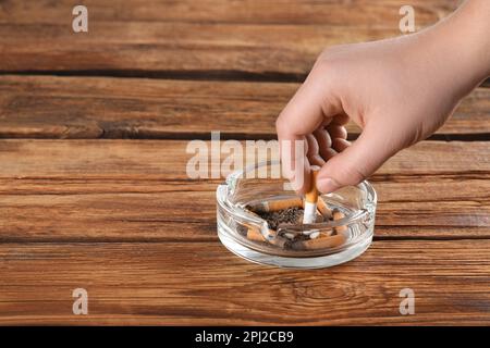 Ein Mann, der Zigaretten im Aschenbecher auf einem Holztisch ausstellt, macht dicht. Platz für Text Stockfoto