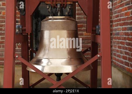 Holzkonstruktion mit großer alter Bronzeglocke in der Nähe von Ziegelmauern im Freien Stockfoto