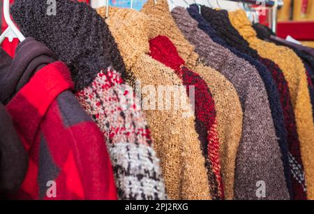 Verschiedene bunte Strickpullover, die an Kleiderbügeln hängen. Mehrfarbige Strickwaren mit Rollkragen, warme Pullover-Kleidung an Kleiderbügeln. Modekonzept. Niemand Stockfoto