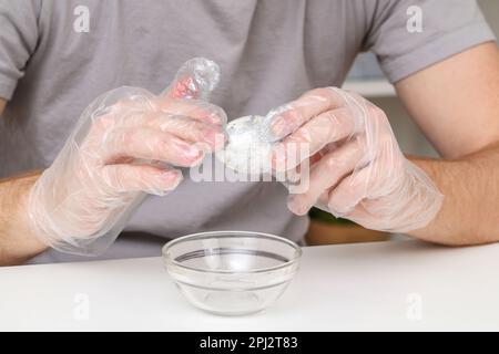 Ein Mann zieht transparente Einweghandschuhe an, um Ostereier zu färben. Färbung von Ostereiern. Stockfoto