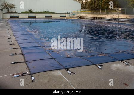 Swimmingpool mit Schmutzabdeckungen. Öffentlicher Swimmingpool mit Poolrutsche, tariert und für den Winter geschlossen. Pool mit Winterdecke für den Herbst. Stockfoto