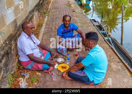 Negombo, Sri Lanka, 13. Februar 2022: Einheimische Fischer essen einen Snack am niederländischen Kanal in Negombo. Stockfoto