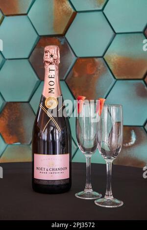 Eine Flasche Moet Rose Imperial, hergestellt vom berühmten französischen Champagnerproduzenten Moet & Chandon, auf einem Tisch mit zwei schlanken leeren Flötengläsern Stockfoto