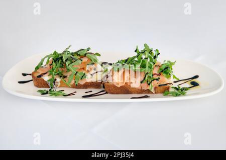 Lachs- und Raketenbruschetta auf einem Tisch zum Servieren, leckeres Essen mit zwei Scheiben Sauerteigbrot, geschmolzenem Mozzarella-Käse und Lachs Stockfoto