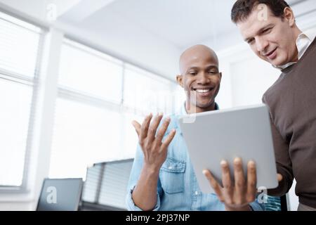 Diese Technologie macht das Leben so einfach. Zwei Geschäftskollegen teilen sich im Büro ein digitales Tablet. Stockfoto