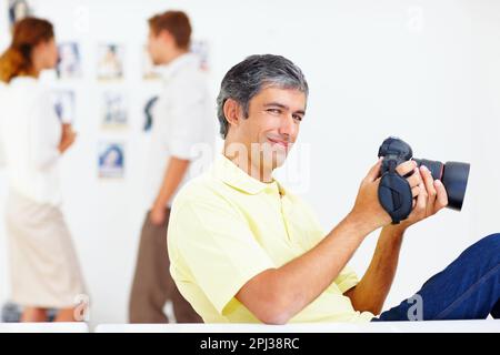 Fotograf, der Fotos in der Kamera ansieht. Porträt eines lächelnden Fotografen, der Fotos in seiner Kamera mit Kollegen im Hintergrund ansieht. Stockfoto