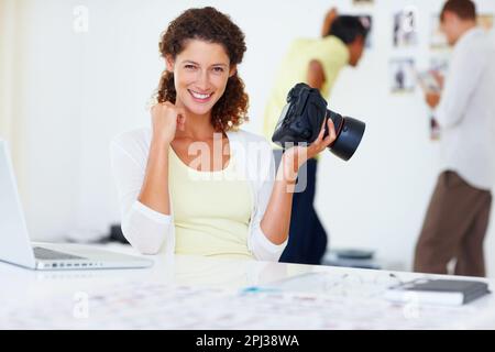 Lächelnde Fotografin. Porträt einer Fotografin, die die Kamera hält und mit Kollegen im Hintergrund lächelt. Stockfoto