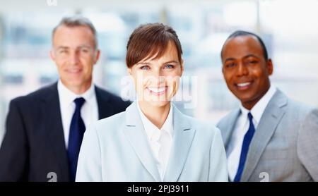Erfolgreiche weibliche Führungskraft mit Kollegen im Hintergrund. Konzentrieren Sie sich auf eine glückliche Geschäftsfrau mit Team im Hintergrund. Stockfoto