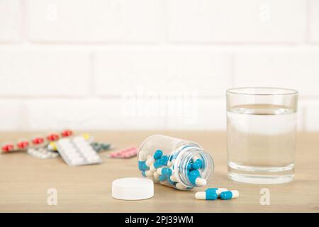 Eine Flasche Pillen und ein Glas Wasser auf hellem Hintergrund. Medizinisches Konzept Stockfoto