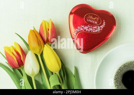 Warschau, Polen - 18. März 2023: Eine Schachtel Lindt-Lindor-Schokolade in einer roten Schachtel in Herzform und frische Blumen. Schokolade mit Kaffee. Schön Stockfoto