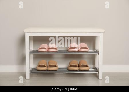 Elegante Aufbewahrungsbank mit verschiedenen Paar Gummipantoffeln an der weißen Wand im Flur Stockfoto