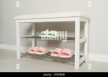 Elegante Aufbewahrungsbank mit verschiedenen Paar Gummipantoffeln an der weißen Wand im Flur Stockfoto