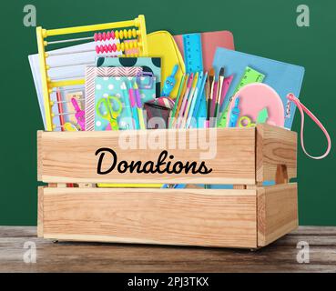 Spendenbox mit unterschiedlichem Schulpapier auf Holztisch in der Nähe der Tafel Stockfoto