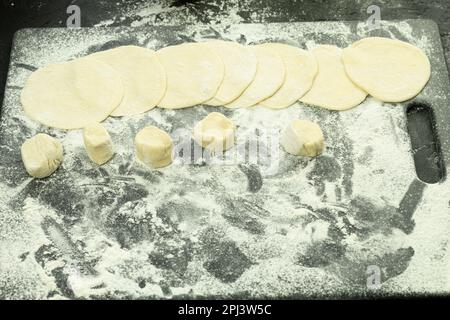 Die Herstellung von Teigtaschen aus Teig. Traditionelles hausgemachtes Essen. Teig für Teigtaschen. Rohe Knödel auf einem Holzbrett. Der Prozess der Herstellung von Dum Stockfoto