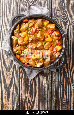 Kalbfleisch-Eintopf mit Gemüsekartoffeln, Karotten, grünen Erbsen, Zwiebeln und Gewürzen in der Nähe in einer Pfanne auf einem Holztisch. Vertikale Draufsicht von oben Stockfoto