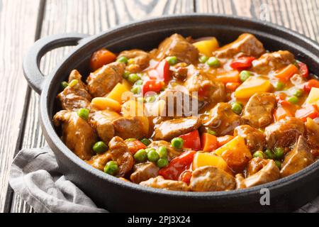 Ein Topf Rindfleisch mit Kartoffeln, Karotten, Tomaten, grünen Erbsen, Zwiebeln mit scharfer Sauce, Nahaufnahme in einer Pfanne auf einem Holztisch. Horizontal Stockfoto