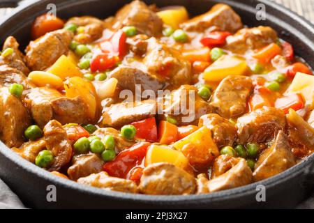 Langsam gekochtes Rindfleisch mit Kartoffeln, Karotten, Tomaten, grünen Erbsen, Zwiebeln und Gewürzen in einer Pfanne auf einem Holztisch. Horizontal Stockfoto