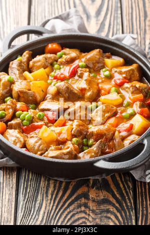 Kalbfleisch-Eintopf mit Gemüsekartoffeln, Karotten, grünen Erbsen, Zwiebeln und Gewürzen in der Nähe in einer Pfanne auf einem Holztisch. Vertikal Stockfoto