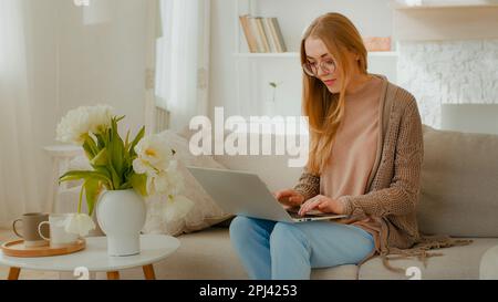 Weiße Frau mit Brille glückliches Mädchen Studentin Geschäftsfrau mit Laptop, die im Heimbüro auf dem Sofa sitzt und online arbeitet Stockfoto