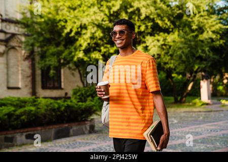 Fröhlicher junger Afro-Mann-Student mit Rucksack, der im Freien auf dem Universitätscampus spaziert Stockfoto