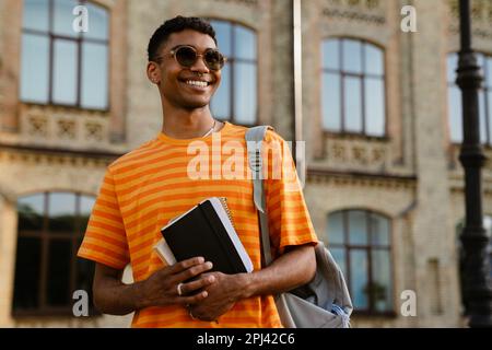 Junger schwarzer brünetter Mann mit Sonnenbrille und Notizblock, während er draußen ist Stockfoto